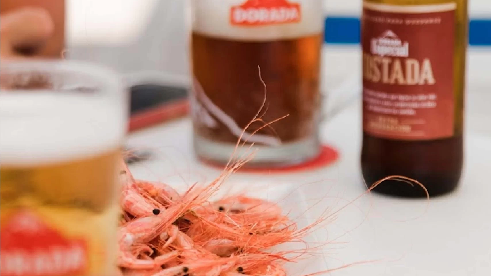 Primer plano de un plato de camarones acompañado de unas cervezas de la marca Dorada.