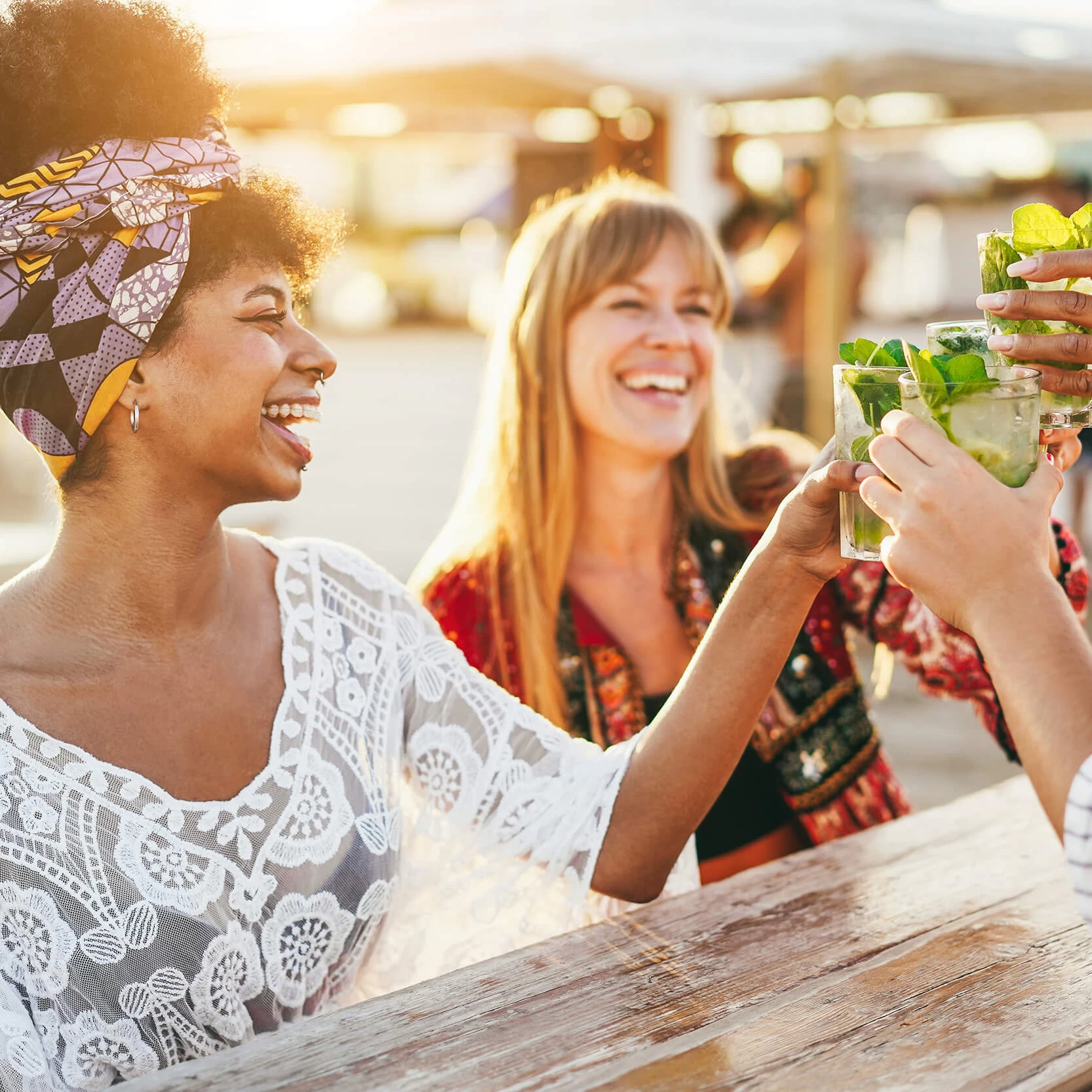 Chicas brindando en la playa sentadas en una mesa.