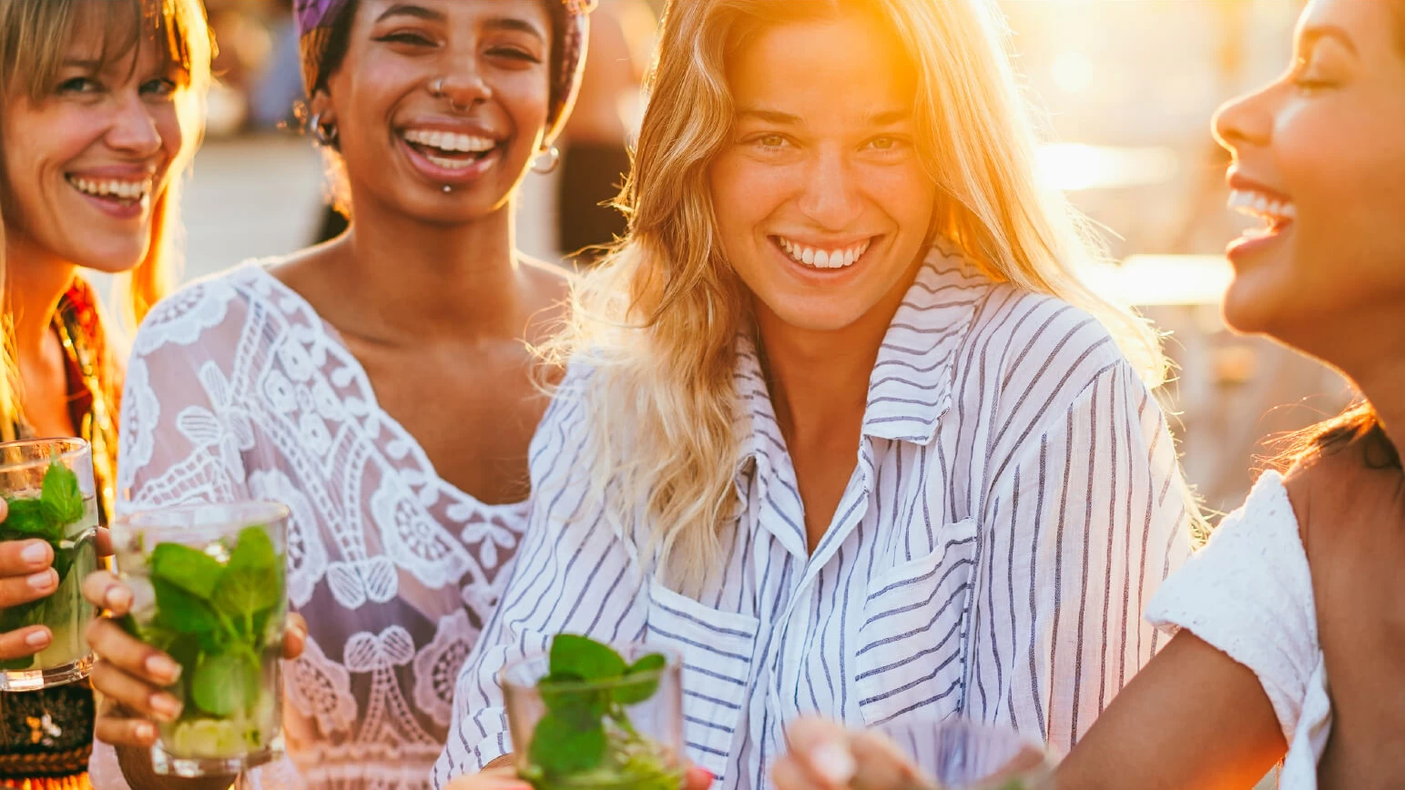 Chicas sonriendo a la cámara con mojitos en la mano.