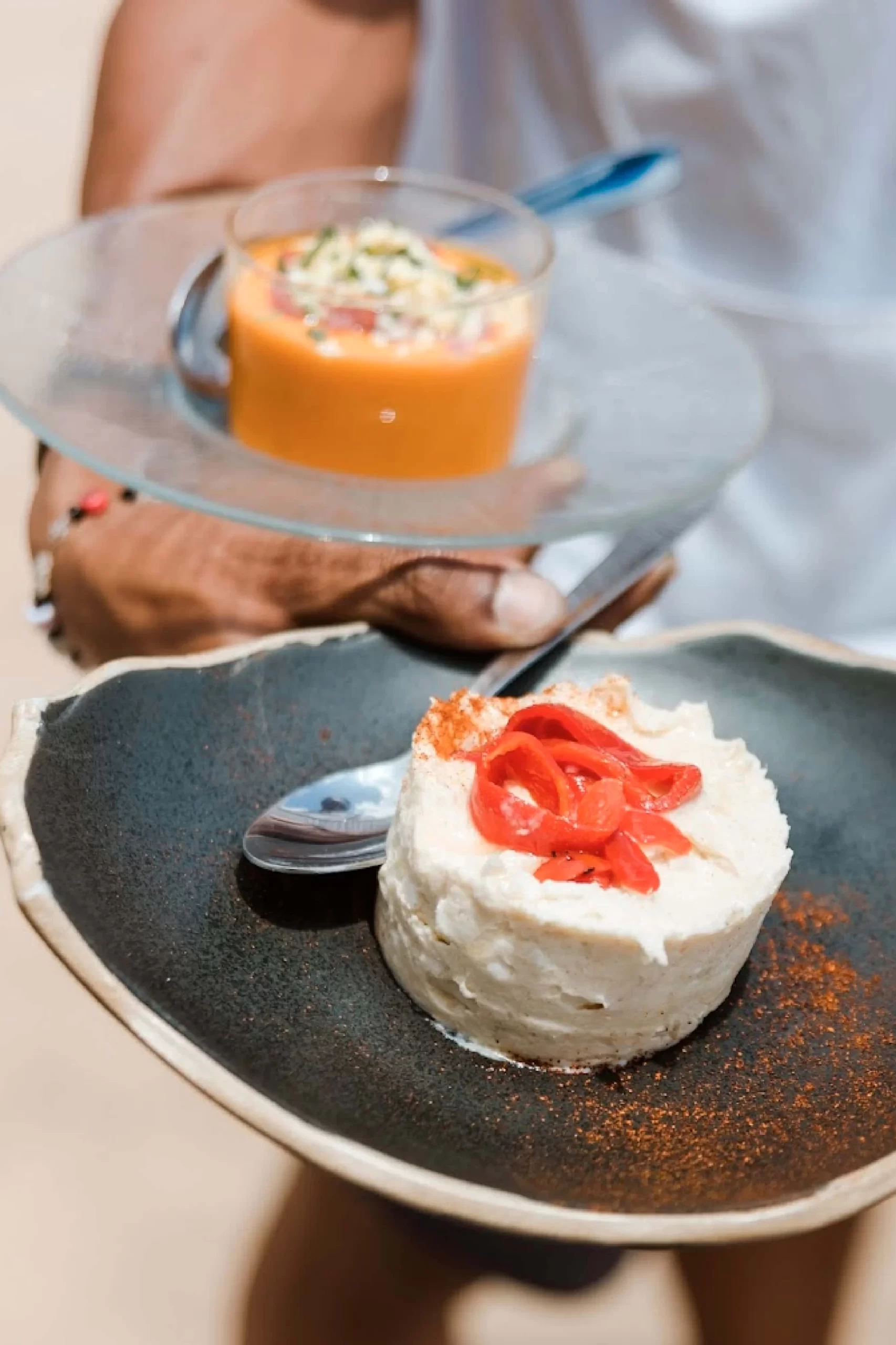 Camarero sostiene un plato de ensaladilla y salmorejo.