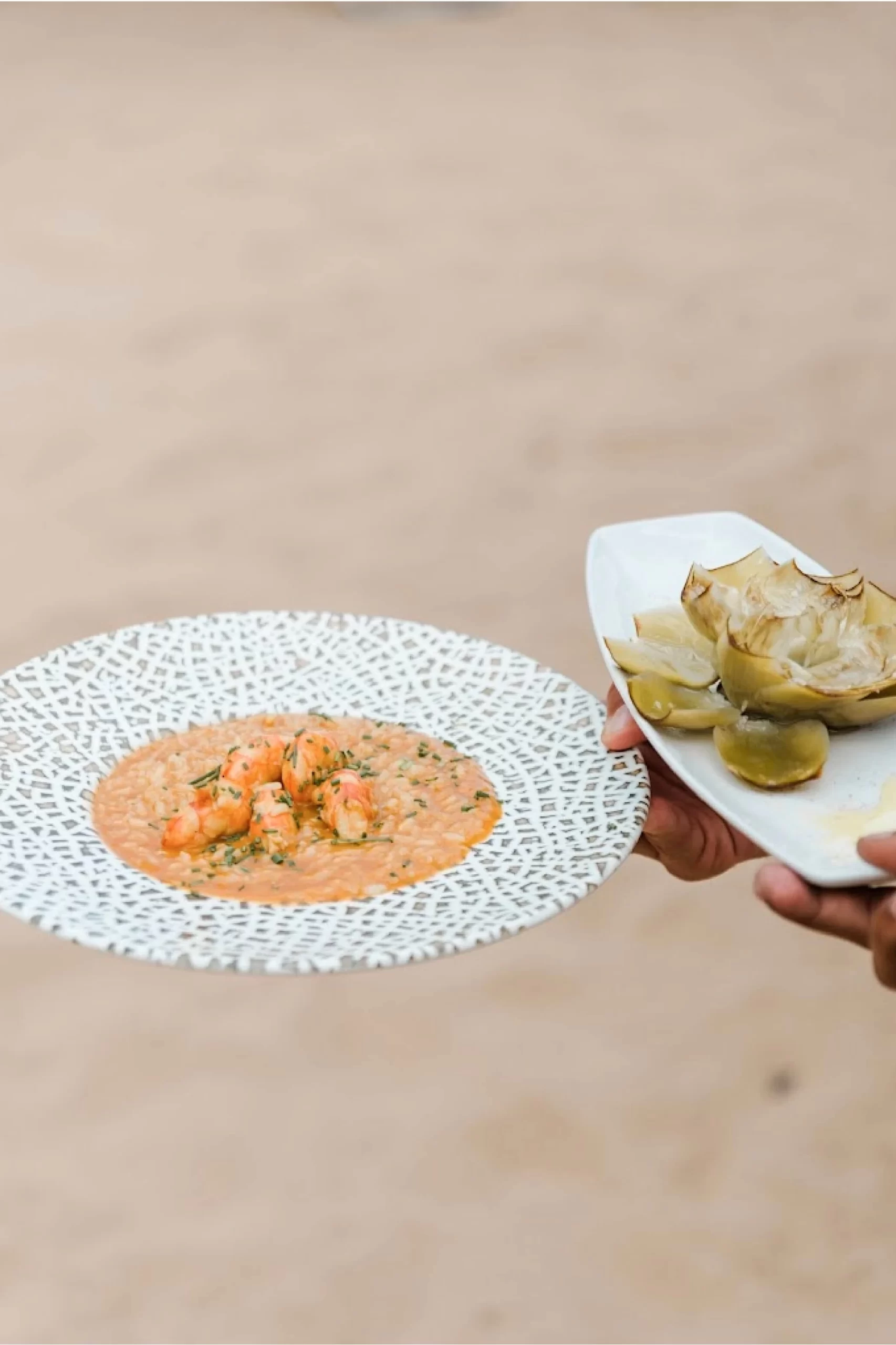 Camarero sostiene un plato de risotto y otro de alcachofa.