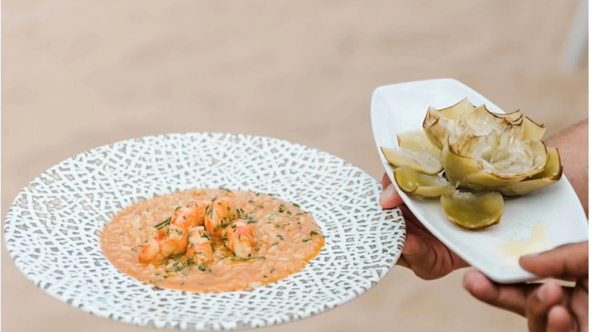 Camarero sostiene un plato de risotto y otro de alcachofa.