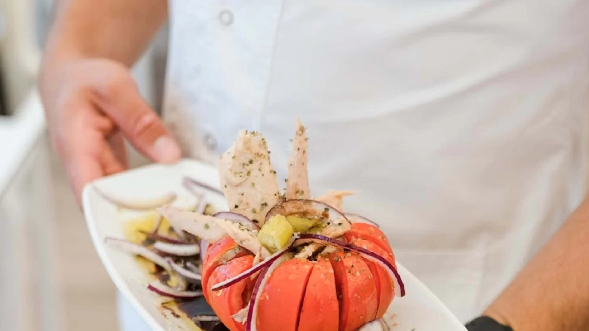 Camarero sostiene un plato con una ensalada aliñada.